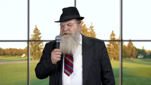 Man Speaking Into a Microphone In Front of Window