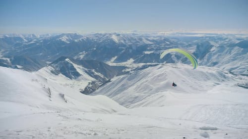 Gleitschirmfliegen über verschneite Berggipfel in den Alpen
