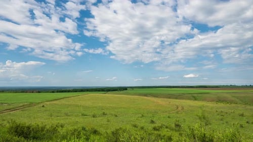 Zeitraffer. Weiße Wolken bewegen sich schnell über den blauen Himmel über grüne Felder