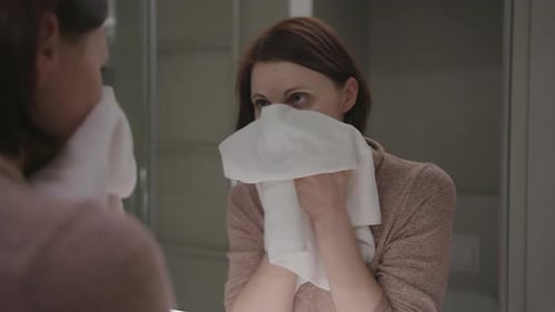 Woman Towels Face in Bathroom Mirror
