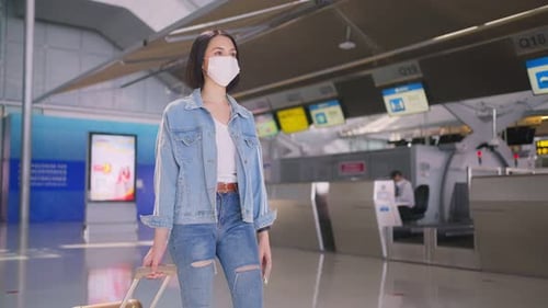 Asian woman passenger wearing face mask, walking in airport terminal to boarding gate to airplane.