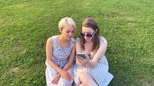 Two Girls in the Park Use a Smartphone and Discuss