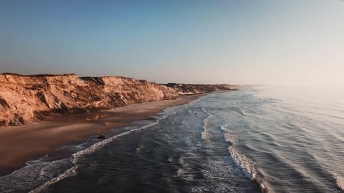 Majestic Aerial Shot of Seaside with Sandy Shores and Waves Crashing Through the Beach