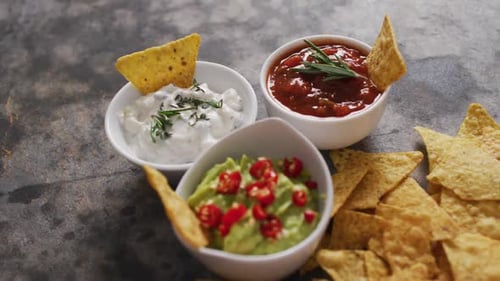 Primer plano de nachos y variedad de salsas sobre una superficie negra