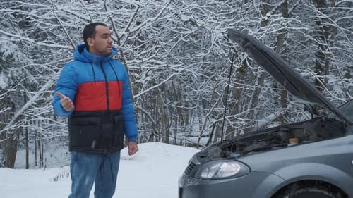 Man Standing on Road Near Broken Car and Trying To Catch Help on Winter Forest Road