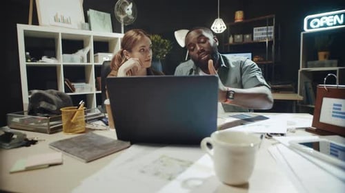 Smiling Afro Man Offering Solution To Businesswoman on Laptop Screen in Office.