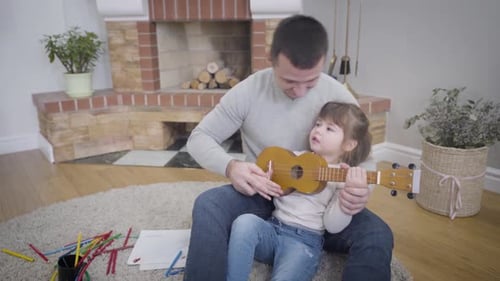 Child and Adult Play Ukulele Together in Home