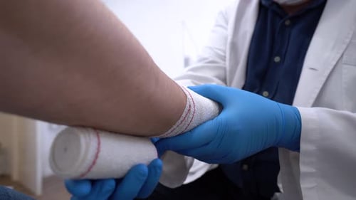 Anonymous doctor bandaging arm of patient in hospital