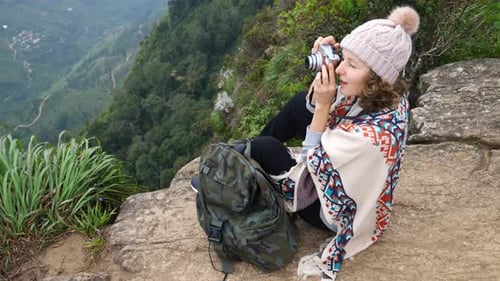Female Hiker With Backpack Take A Photograph Sitting On The Edge Of Cliff