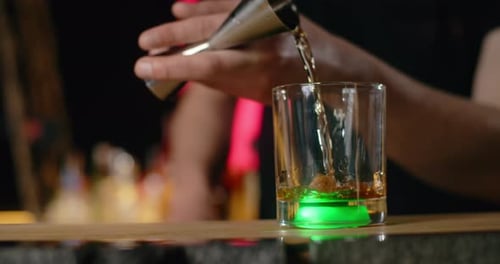 Barman Pours Portion of Alcohol From Jigger to the Glass with Green Backlight in Slow Motion Making