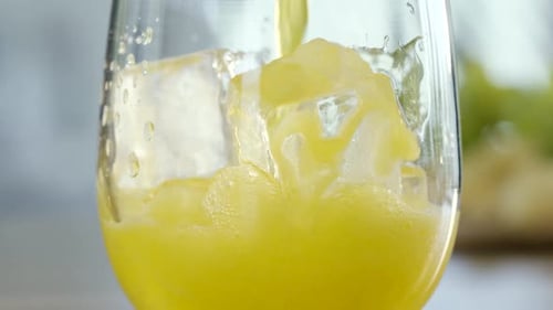 Yellow Juice Pouring into Glass with Ice