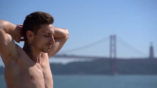 Shirtless Man Stretching on Sunny Day Near Ocean