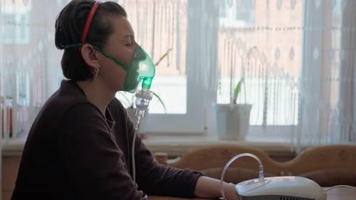 Une femme européenne à la maison effectue une inhalation de vapeurs d'huile oxygène à travers un masque