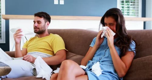 Couple se mouchant dans un mouchoir en papier dans le salon de la maison
