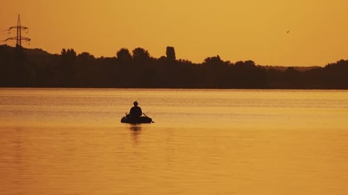Boot mit einem Fischer im Sonnenuntergangslicht schwebt langsam auf dem See.