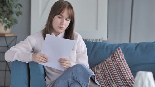 Woman Reads Documents on Couch at Home