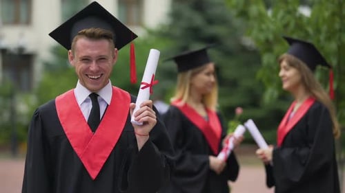 Joyful Male Graduate Holding Diploma in His Hand and Smiling, Happy Moment