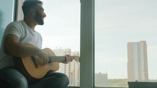 Man Plays Acoustic Guitar in Urban Apartment