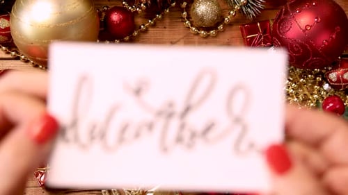 Hands put a Christmas card with text DECEMBER close to camera