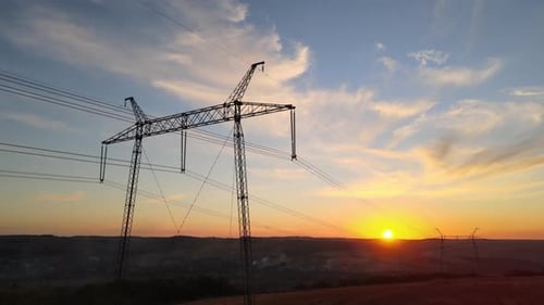 Dark Silhouette of High Voltage Tower with Electric Power Lines at Sunrise