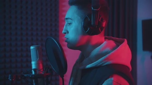 A Man in Headphones Rapping Through the Pop-filter in the Microphone - Studio in Neon Lighting