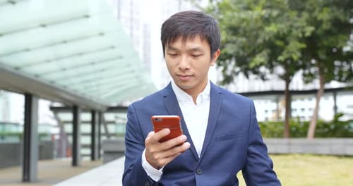 Man in Suit Looks at Mobile Phone Outside