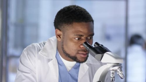 Glücklicher afroamerikanischer Laborassistent bei der Arbeit mit Mikroskop