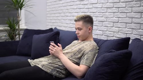 Young Adult Relaxing on Couch Using Smartphone
