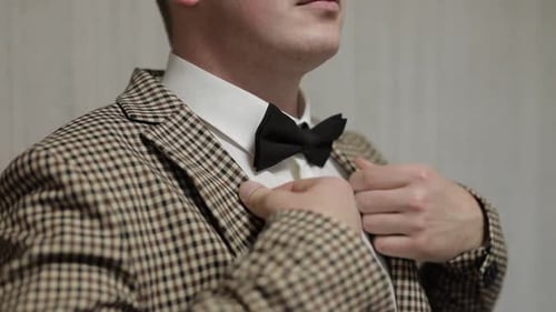 Man adjusts bowtie and checkered jacket