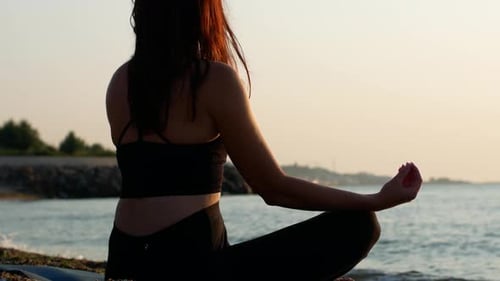 Une femme yogi est assise en position de lotus au bord de la mer et regarde l'aube du soleil.