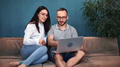 Woman and Man Looking at Laptop on Sofa