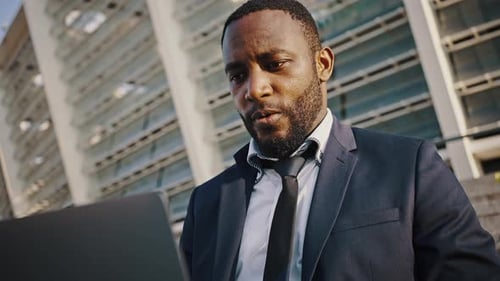 Serious Focused African American Businessman Typing on Laptop Working Remotely Near Business Center