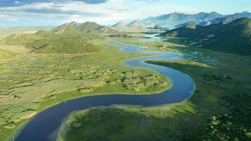 Bends and curves of blue river flowing through green valley toward distant mountains.
