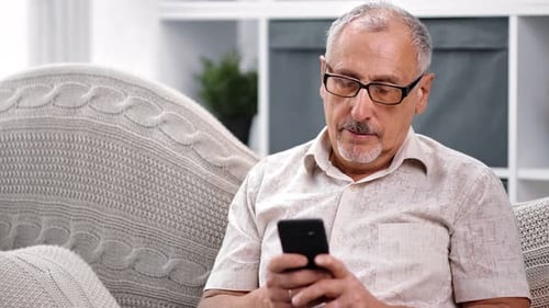 Senior Man Using Smartphone While Relaxing Indoors
