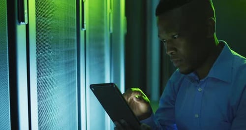 Young Adult Works in a Green Lit Server Room