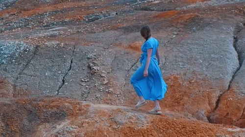 Woman in Blue Dress Walking on Rocky Hills