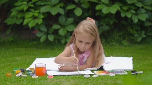 Girl Drawing on Grass with Watercolors in Summer