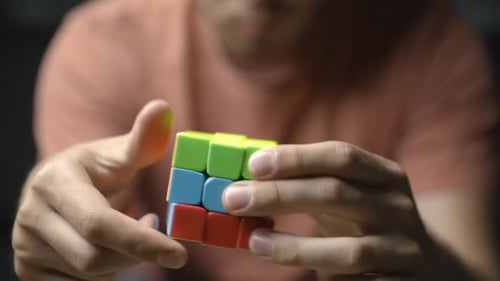 Close-up da frente de jovens mãos masculinas resolvendo o cubo colorido de Rubik