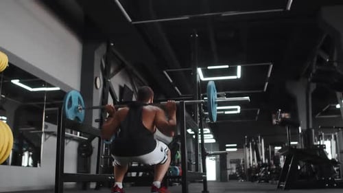 Muscular Man Training with Barbell Doing Squats in Gym Back View