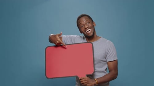 Happy Adult Pointing at Cardboard Speech Bubble in Studio