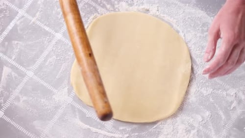 Hands Rolling Dough on Floured Surface