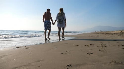 Couple of Lovers Walking at Seashore Holding Hands During Recreation on Resort. Man and Woman
