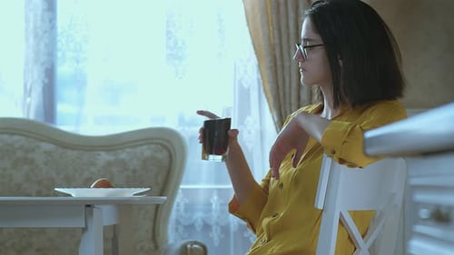 Una chica morena con gafas se sienta en una mesa y bebe una bebida de un vaso para saciar su sed