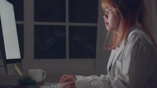Young asian woman working late using desktop on desk in living room at home