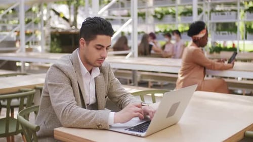 Man Typing on Laptop at Outdoor Cafe