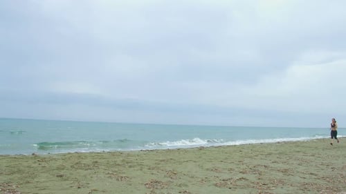 Woman Running Along Sandy Beach on Overcast Day