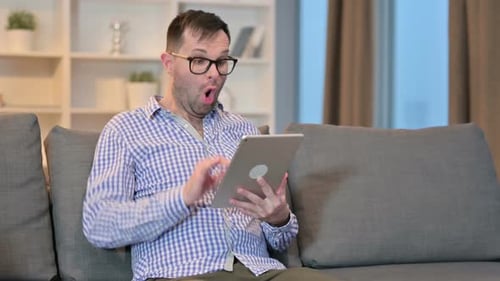 Man Celebrates Success on Tablet at Home