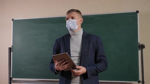 Young Male Teacher in a Medical Mask on His Face at School Near the Blackboard