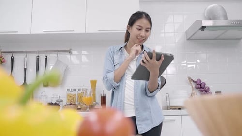 Happy Asian woman using tablet for looking recipe while making food.