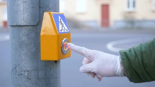 Une main dans un gant appuie sur le bouton du passage pour piétons au feu de signalisation en gros plan, protection contre le coronavirus